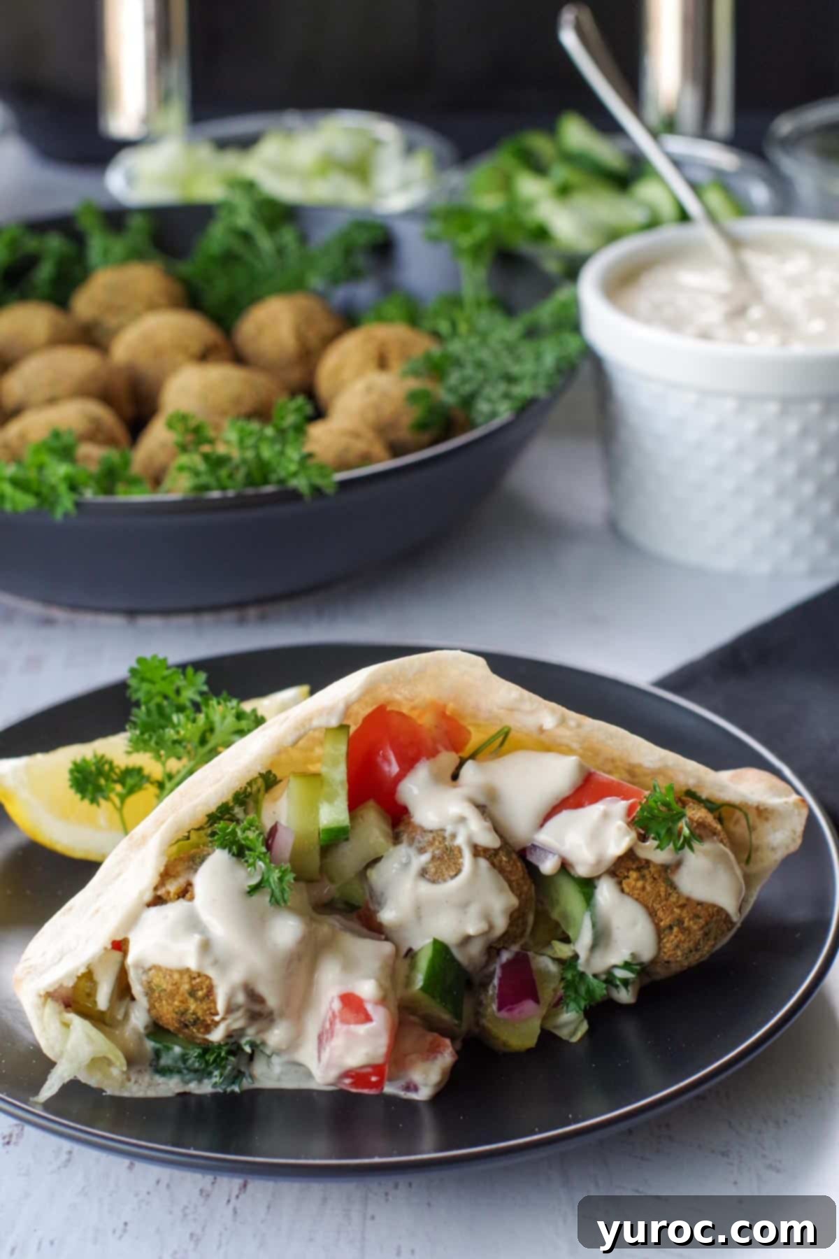 Crispy Air Fryer Falafel from Mix 13 air fryer falafel in pita on black plate, with bowl of falafel balls and pita in the background