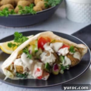 Crispy Air Fryer Falafel from Mix 14 air fryer falafel pita on a black plate with a bowl of falafel balls in the background