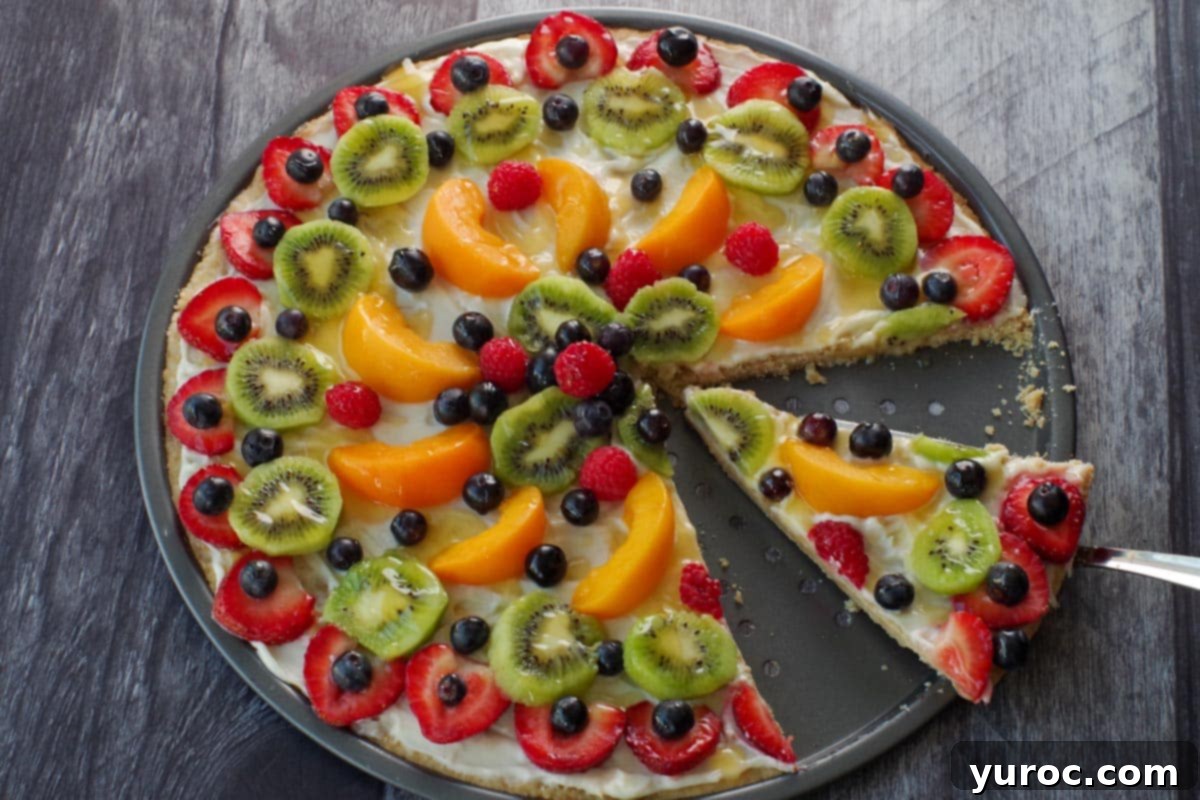 Vibrant Fruit Pizza with Sweet Glaze 1 A slice of vibrant fruit pizza being lifted from a larger pizza, showcasing the creamy topping and colorful fresh fruits.