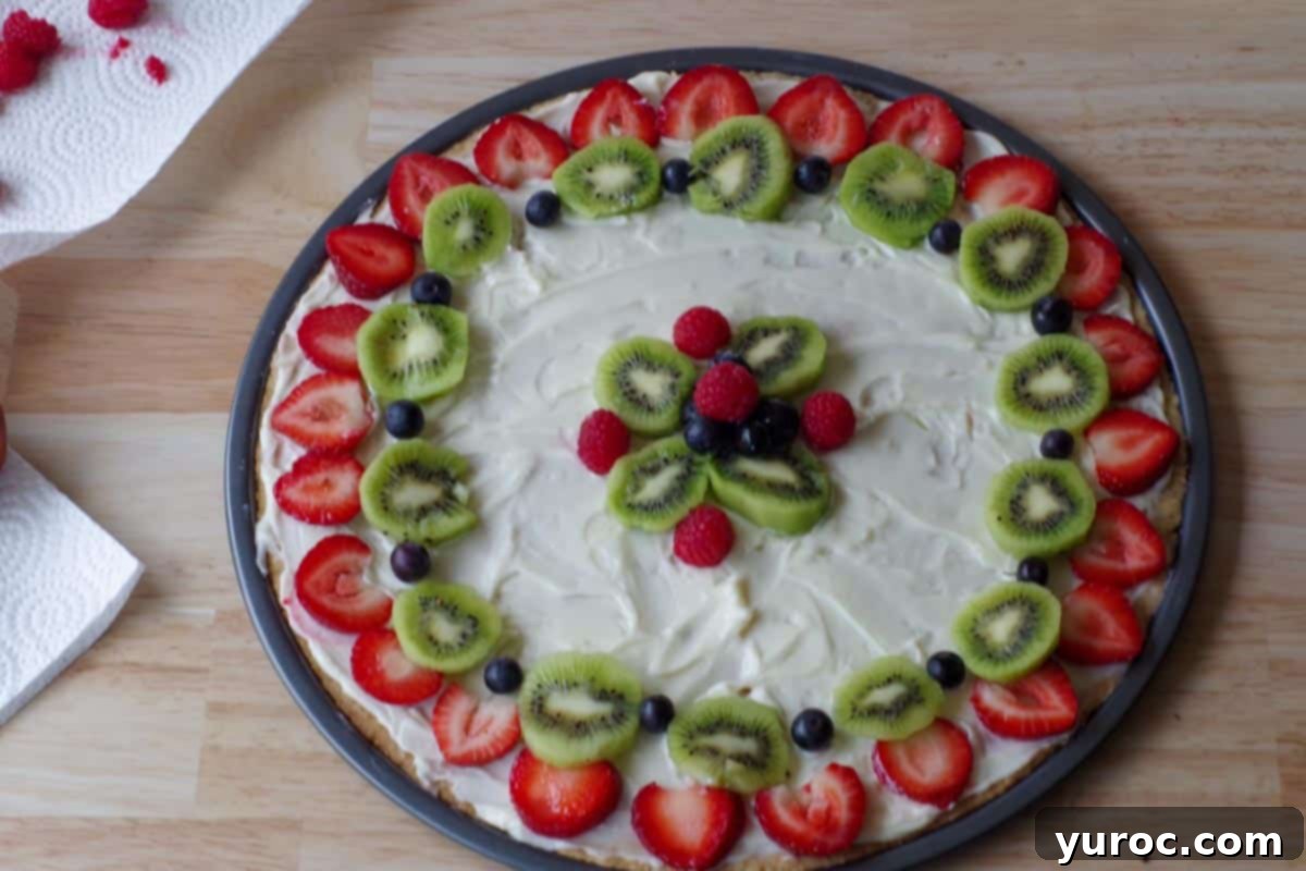 Vibrant Fruit Pizza with Sweet Glaze 11 A fruit pizza partially decorated, with fresh strawberries, blueberries, and kiwi arranged beautifully around the outer edge, leaving the center open.
