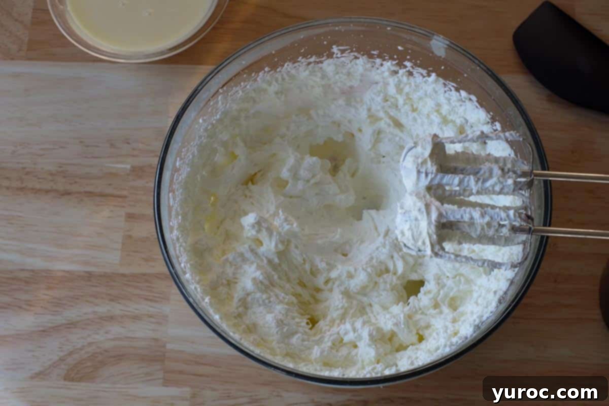 Vibrant Fruit Pizza with Sweet Glaze 8 Softened cream cheese and white sugar being beaten together in a glass bowl with an electric mixer until perfectly smooth.