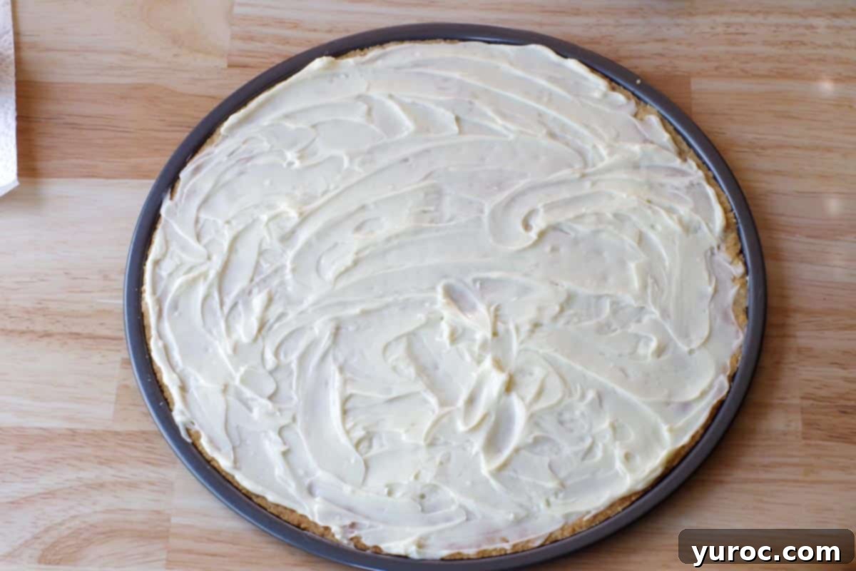 Vibrant Fruit Pizza with Sweet Glaze 9 The creamy white cream cheese topping spread smoothly and evenly over the cooled shortbread crust, ready for fruit decoration.