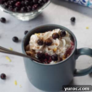 Saskatoon berry crisp recipe in a mug with a spoon in it, berries stewn around and a bowl of Saskatoon berries in the background