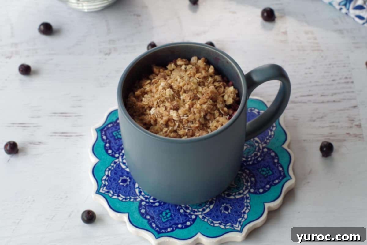 cooked Saskatoon berry crisp in a mug, sitting on a trivet, with Saskatoon berries strewn around