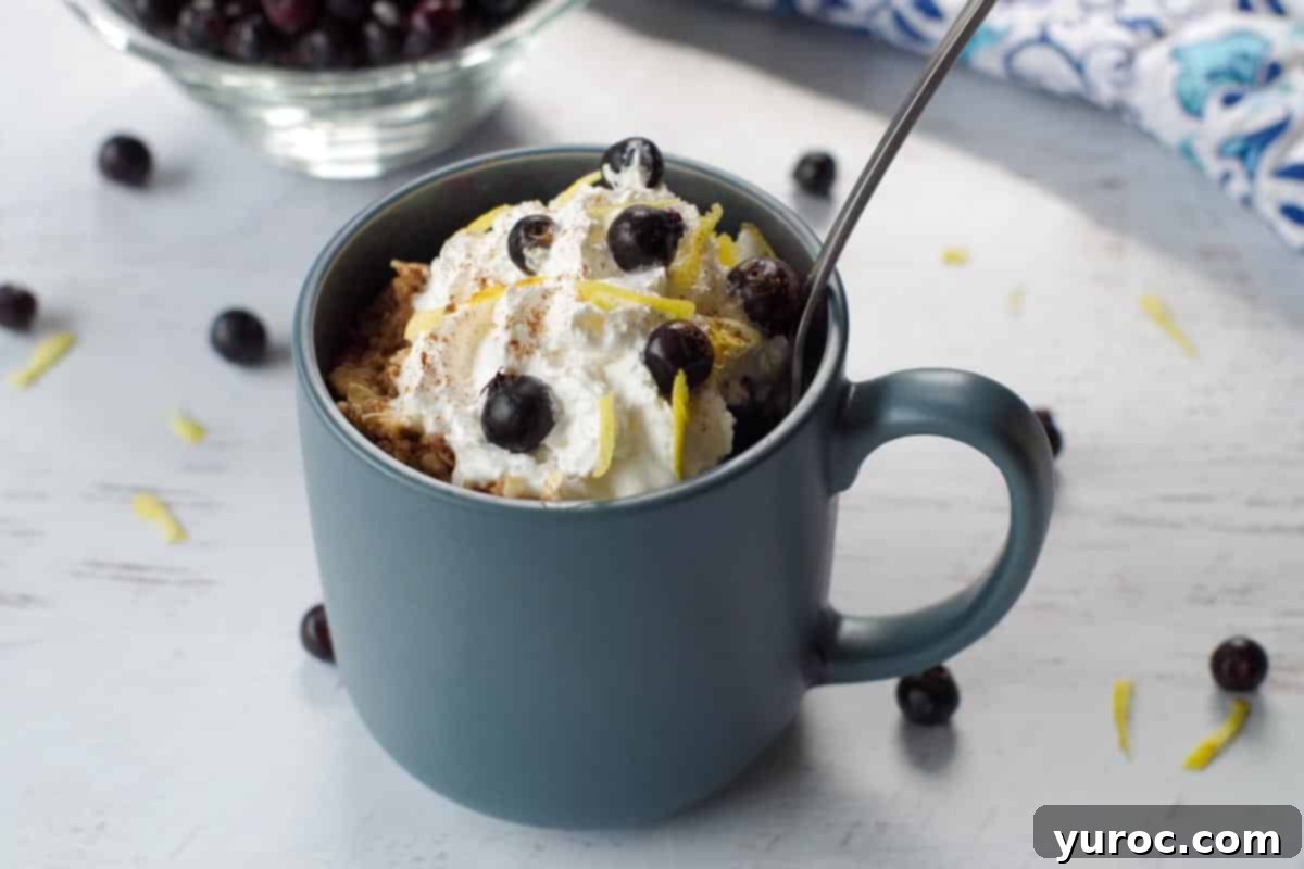 Saskatoon berry crisp recipe in a mug with a spoon in it, berries stewn around and a bowl of Saskatoon berries in the background