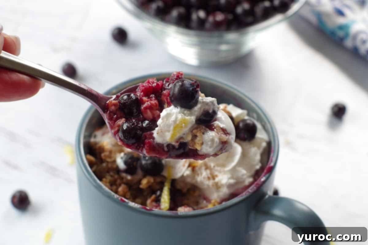Saskatoon crisp being held up on a spoon over a mug of more Saskatoon berry crisp