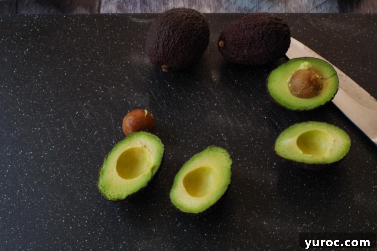 Fresh avocados sliced in half on a black cutting board, with the pits removed and a knife resting nearby