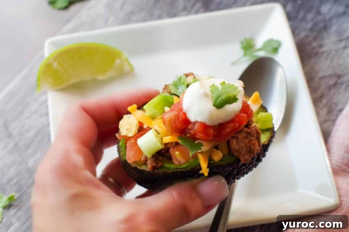 A hand gently holding up a fully assembled avocado taco over a pristine white plate, showcasing its vibrant toppings