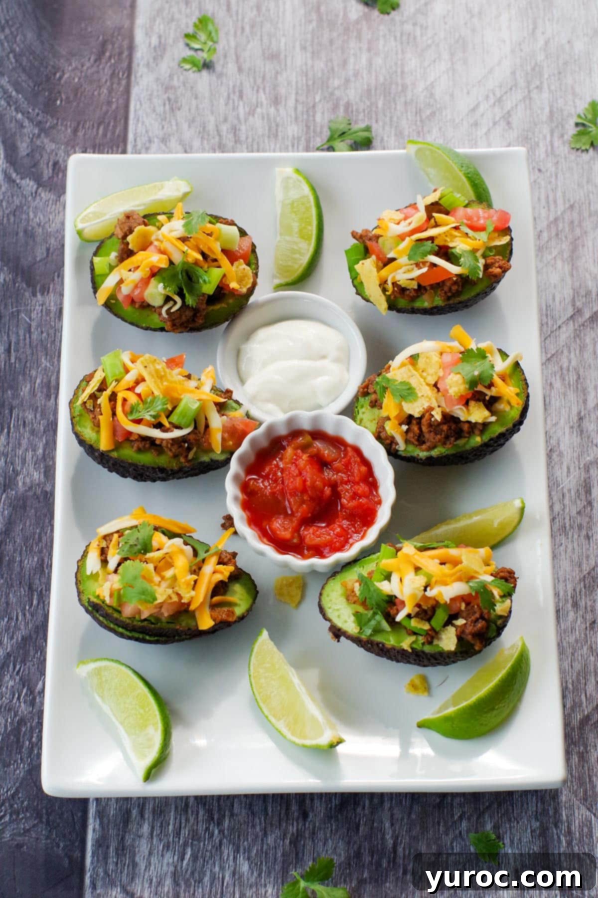 A white serving tray elegantly presenting multiple avocado tacos, centered with bowls of fresh salsa and creamy sour cream, and garnished with bright lime wedges