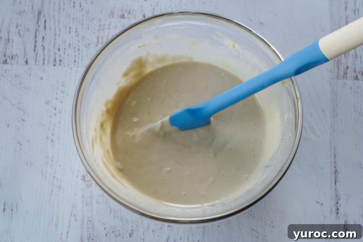 Creamy tahini sauce in a clear glass bowl, with a blue rubber spatula resting in it, highlighting its smooth and thick texture, ready for serving or storage.