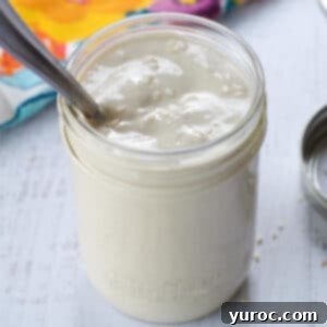 Tahini sauce in a glass jar with a spoon in it