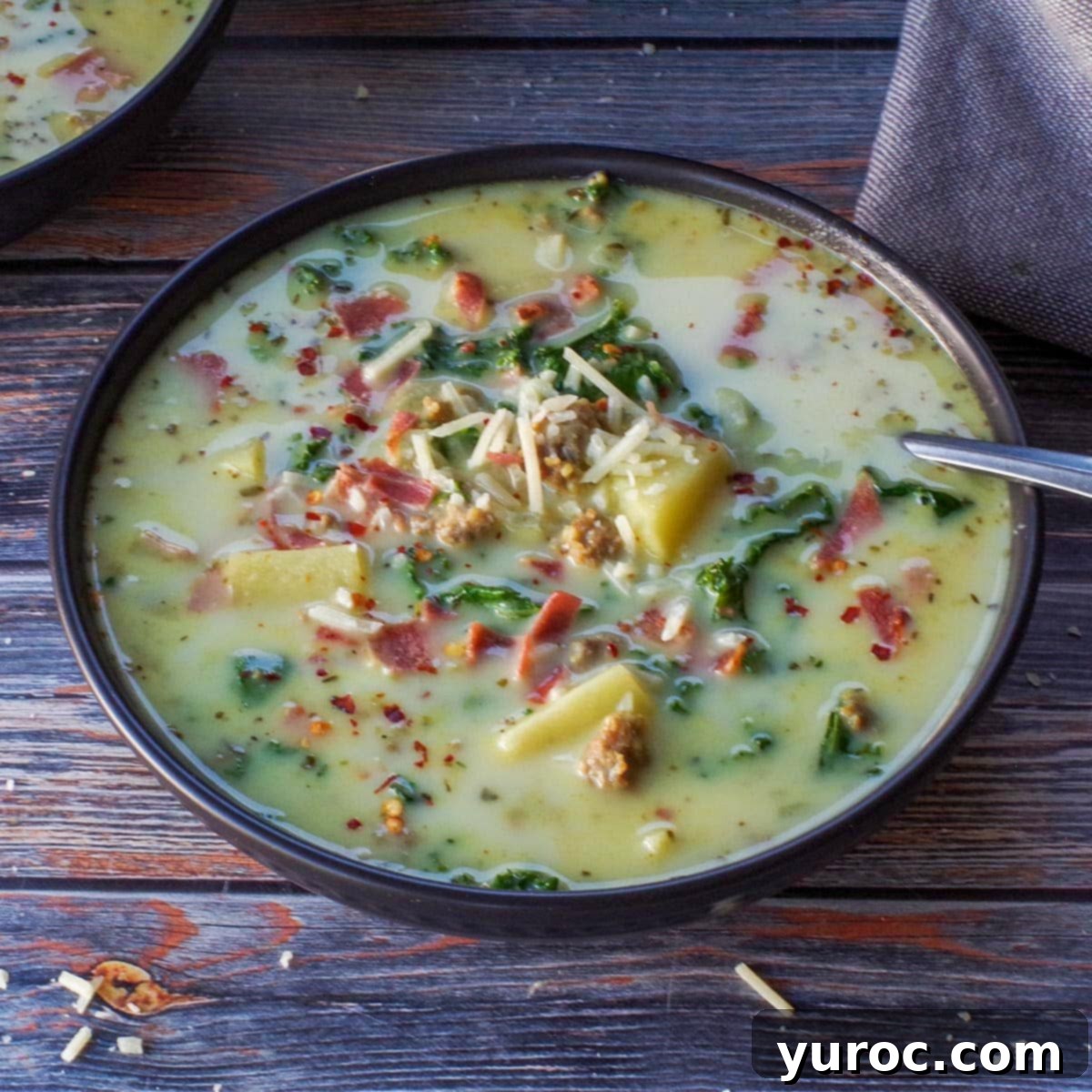 slow cooker zuppa toscana in a black bowl with a spoon, garnished with turkey bacon and red pepper flakes