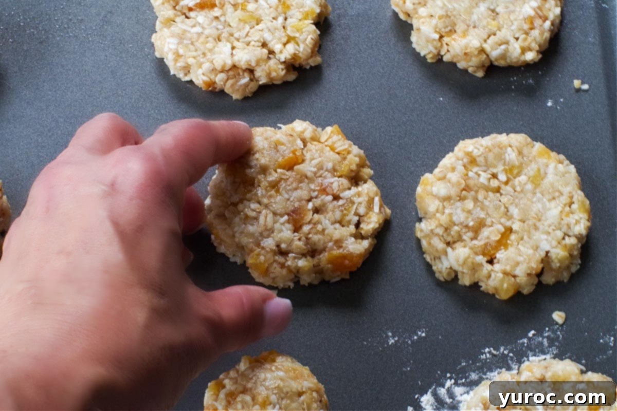 Oatmeal cookies on a baking sheet, with a hand gently touching the edges of a cookie to ensure it's set