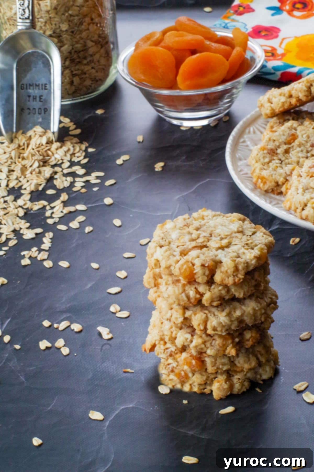 A stack of Oatmeal Apricot cookies, with more cookies on a white plate in the background, illustrating convenient storage and display