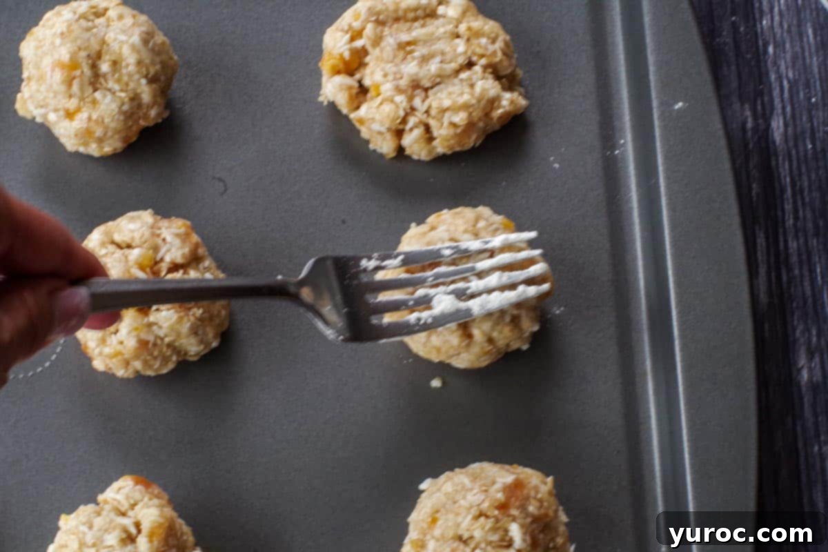 A flour-dipped fork gently pressing down on a cookie dough ball on a baking sheet, flattening it before baking