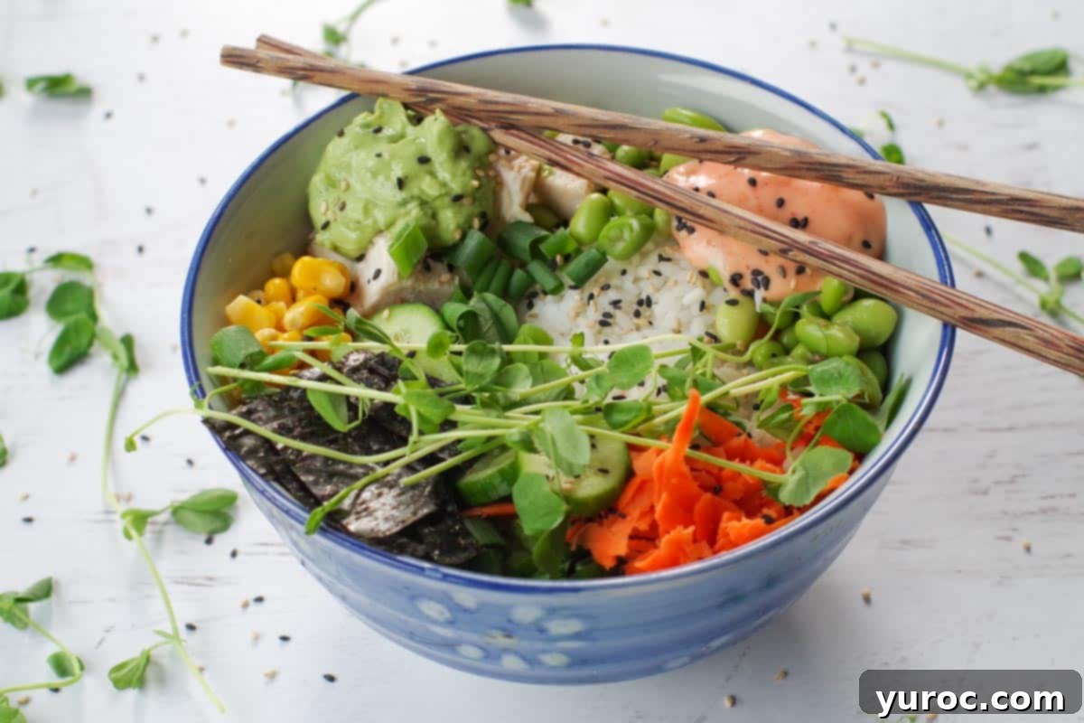 A vibrant chicken poke bowl with chopsticks resting over the rim and fresh pea shoots artfully scattered around.