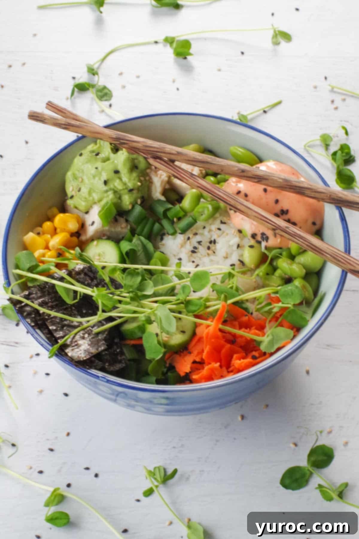 A close-up shot of a chicken poke bowl with chopsticks elegantly placed over the top, surrounded by fresh pea shoots, emphasizing its vibrant presentation.