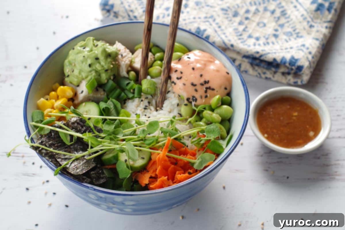 A beautifully arranged chicken poke bowl with chopsticks, accompanied by a small white dish of miso salad dressing, set against a patterned tea towel.