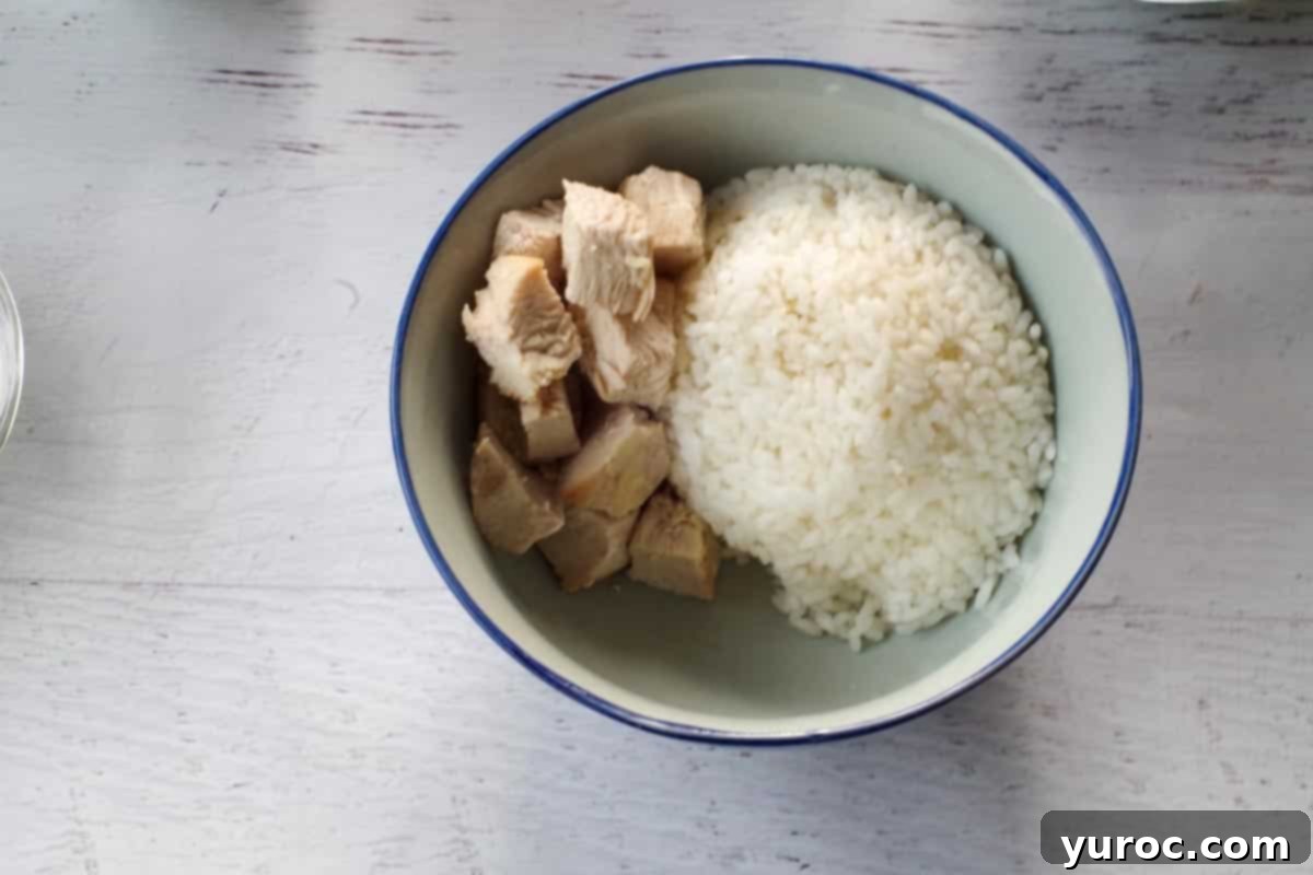 Cooked and diced chicken pieces added alongside the sushi rice in the bowl, creating the protein base.