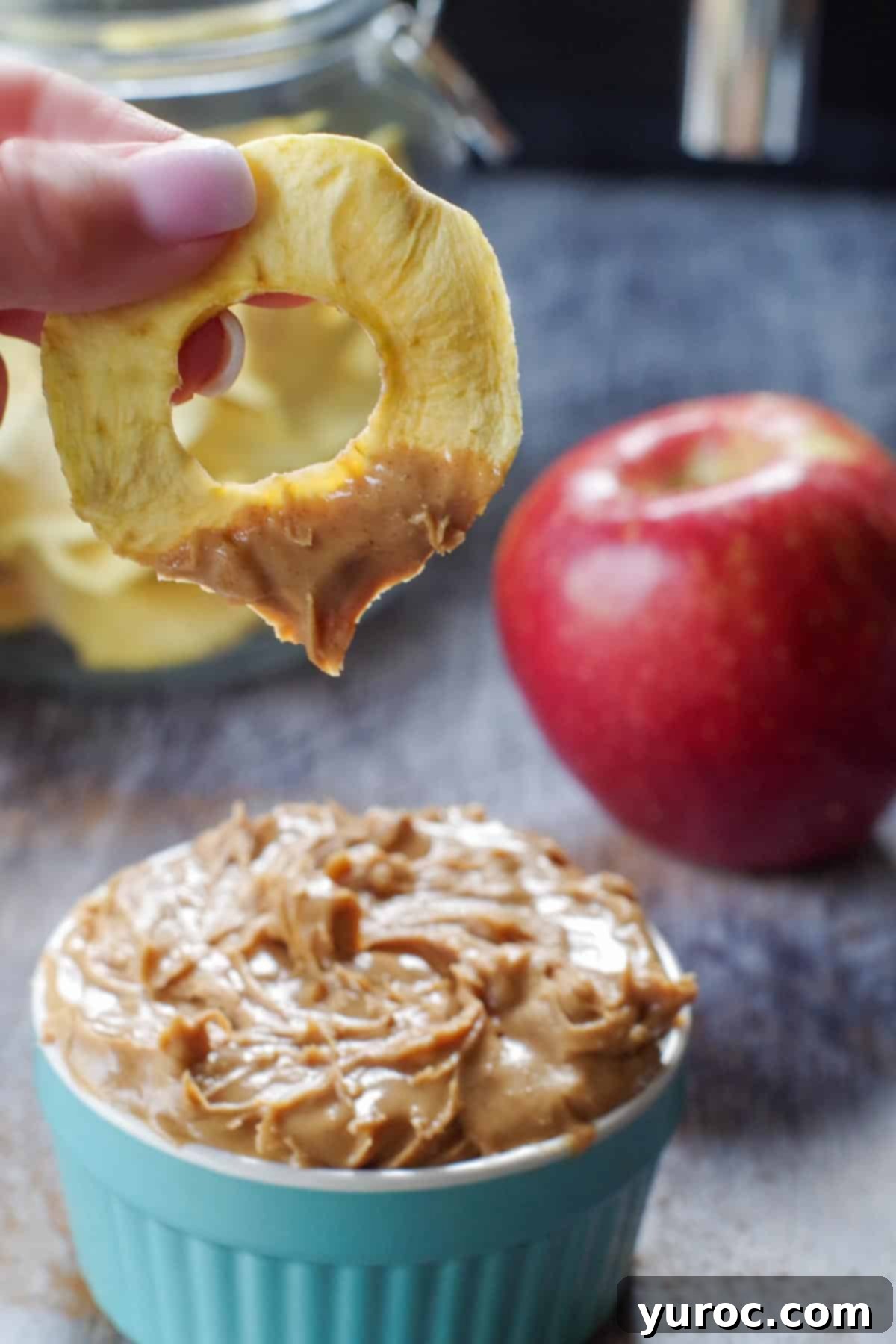 air fryer dehydrated apple being dipped into a small container of peanut butter
