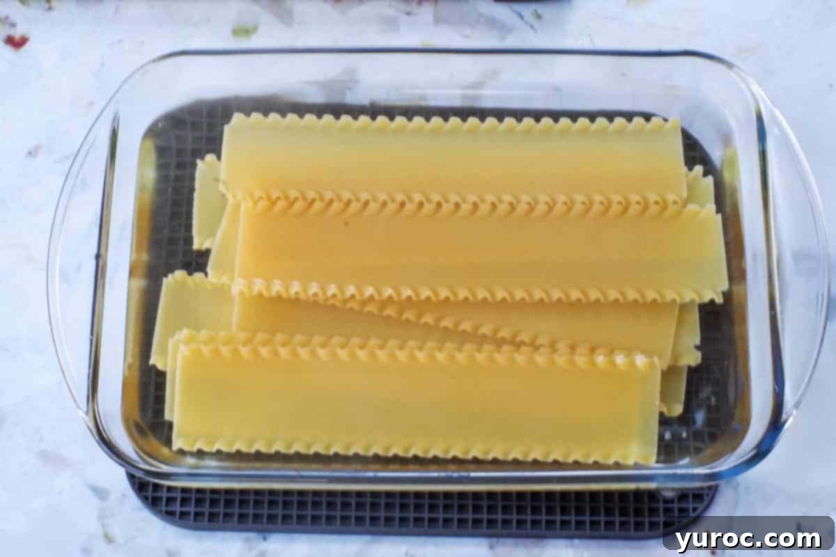 Oven-ready lasagna noodles soaking in boiling water in a 9x13 pan
