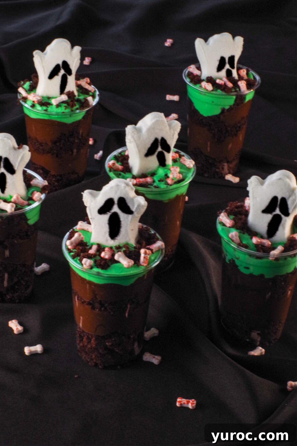 Six more Boo! Halloween Dessert Cups beautifully arranged on a black surface, with additional candy bloody bones scattered around, showcasing the finished product.