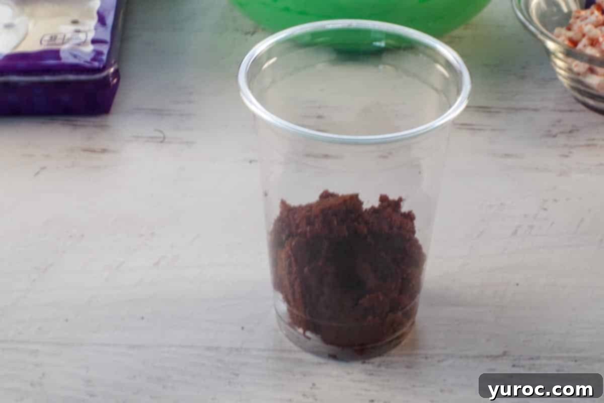 Clear plastic cup with broken-up chocolate cake forming the bottom layer, ready for the next ingredient.