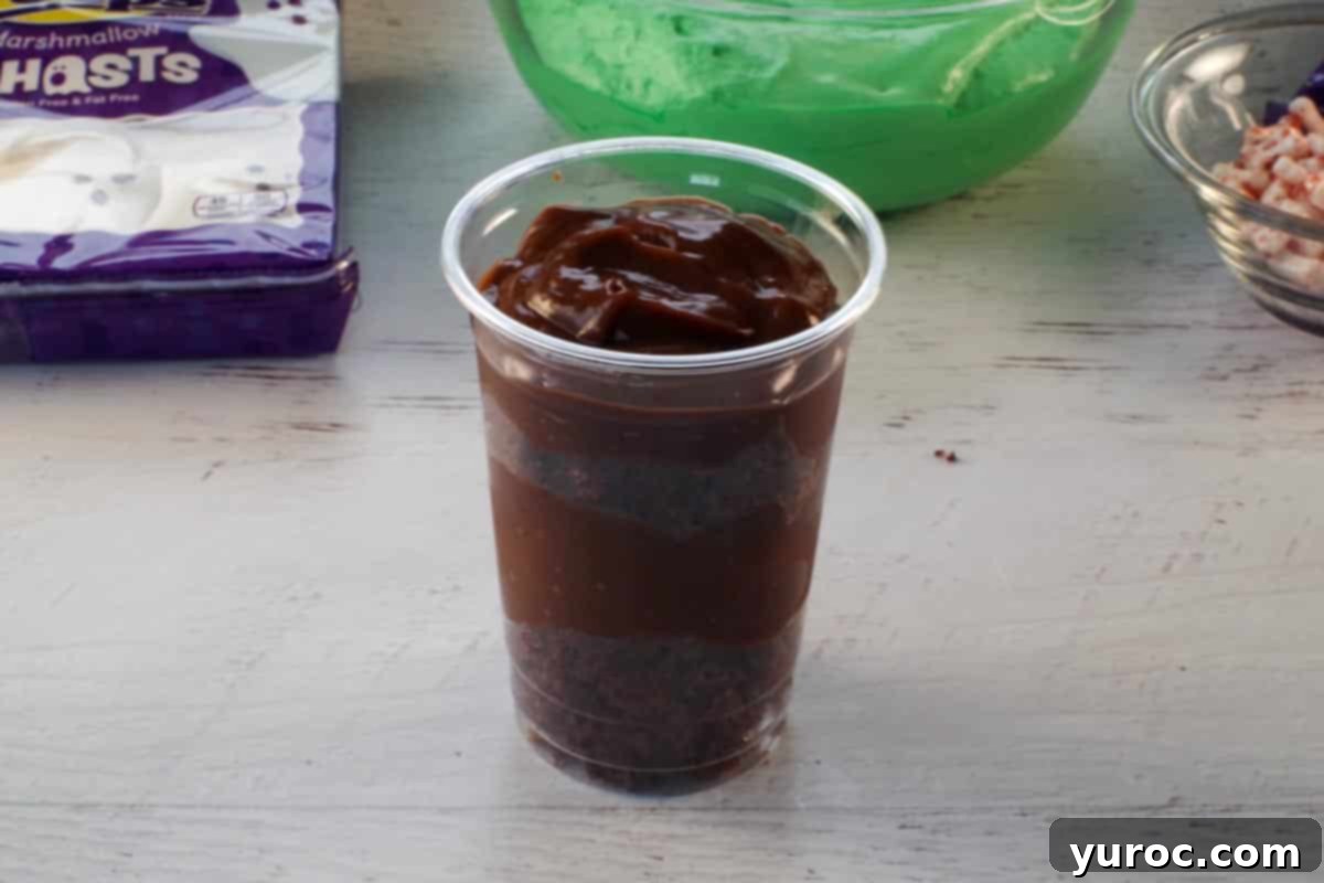 The final layer of chocolate pudding is added, covering the second cake layer in the dessert cup.