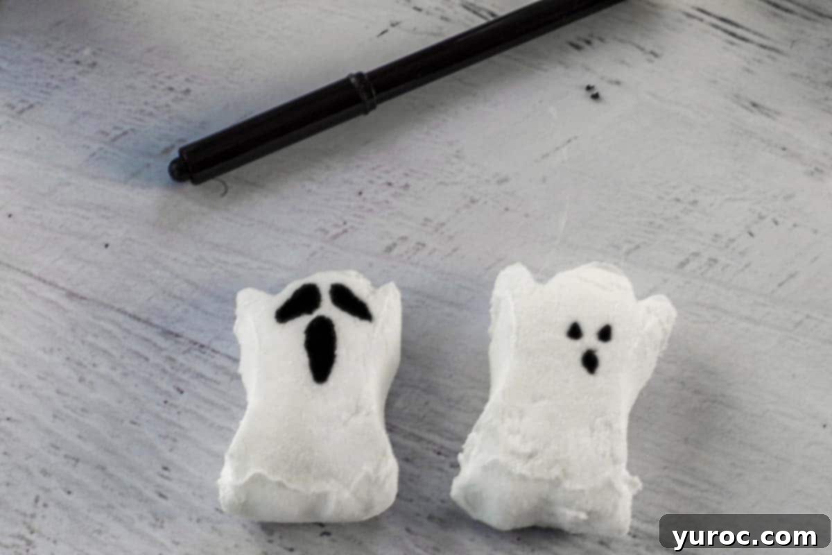 Two ghost peeps, one with a regular face and one with a scarier, drawn face, with an edible black marker in the background.