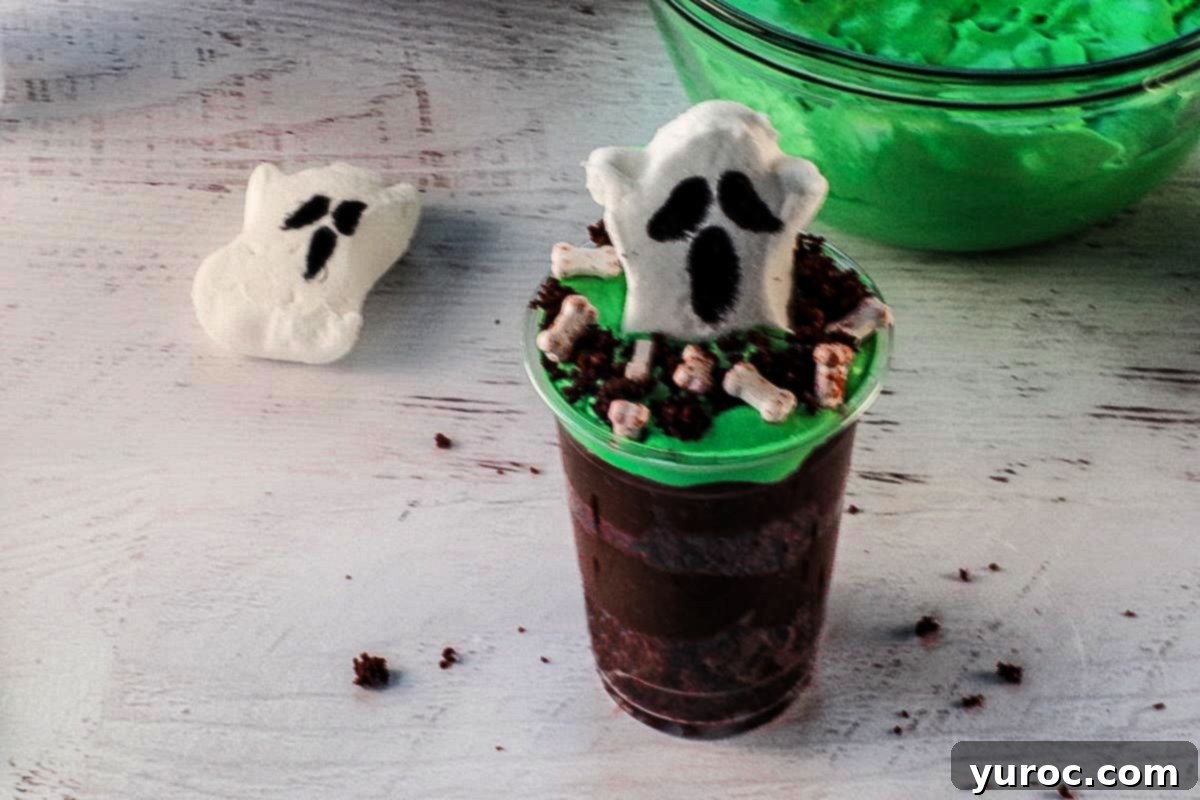 A decorated ghost peep is placed in the middle of a dessert cup, surrounded by scattered cake crumbs and several candy bloody bones, creating a graveyard scene.