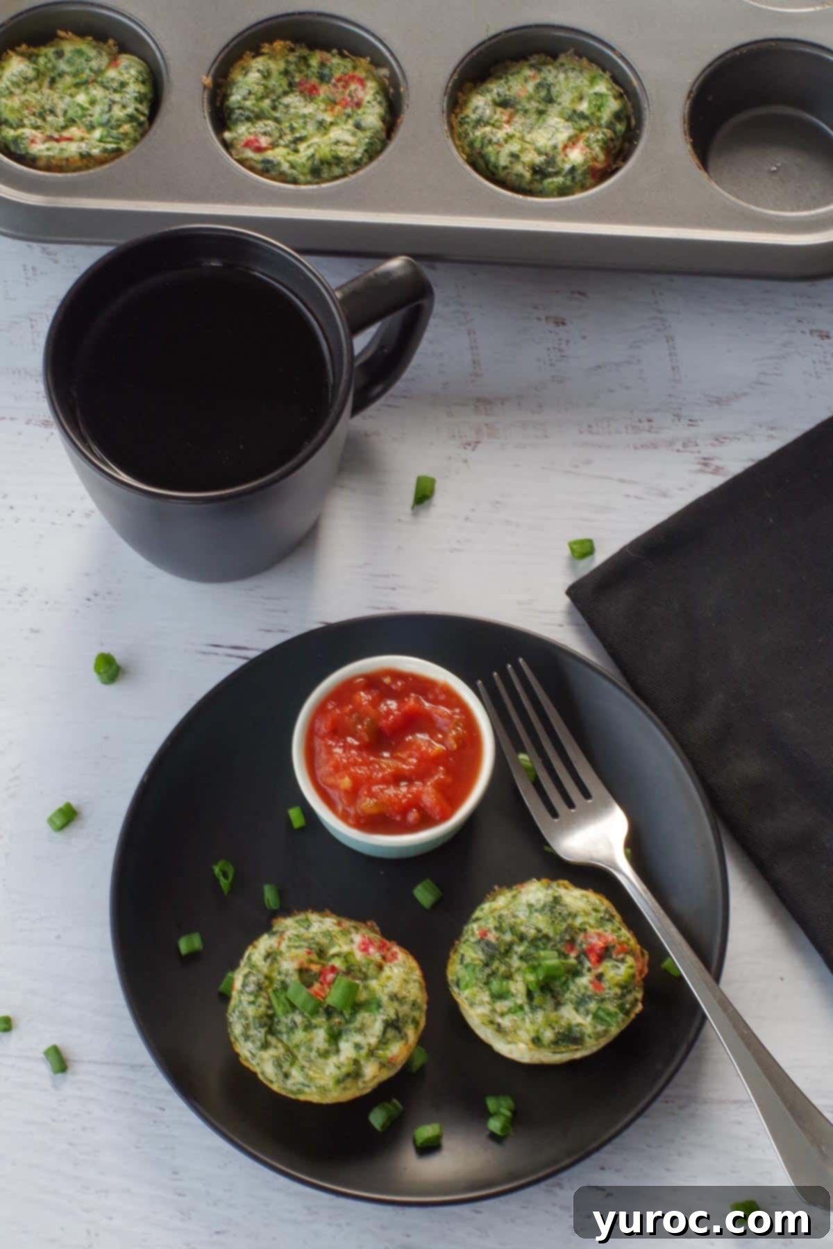 Vibrant Roasted Red Pepper Egg White Bites 12 2 egg white bites on a black plate, with salsa in a small dish, a fork on the plate and a muffin tin with more egg bites in the background