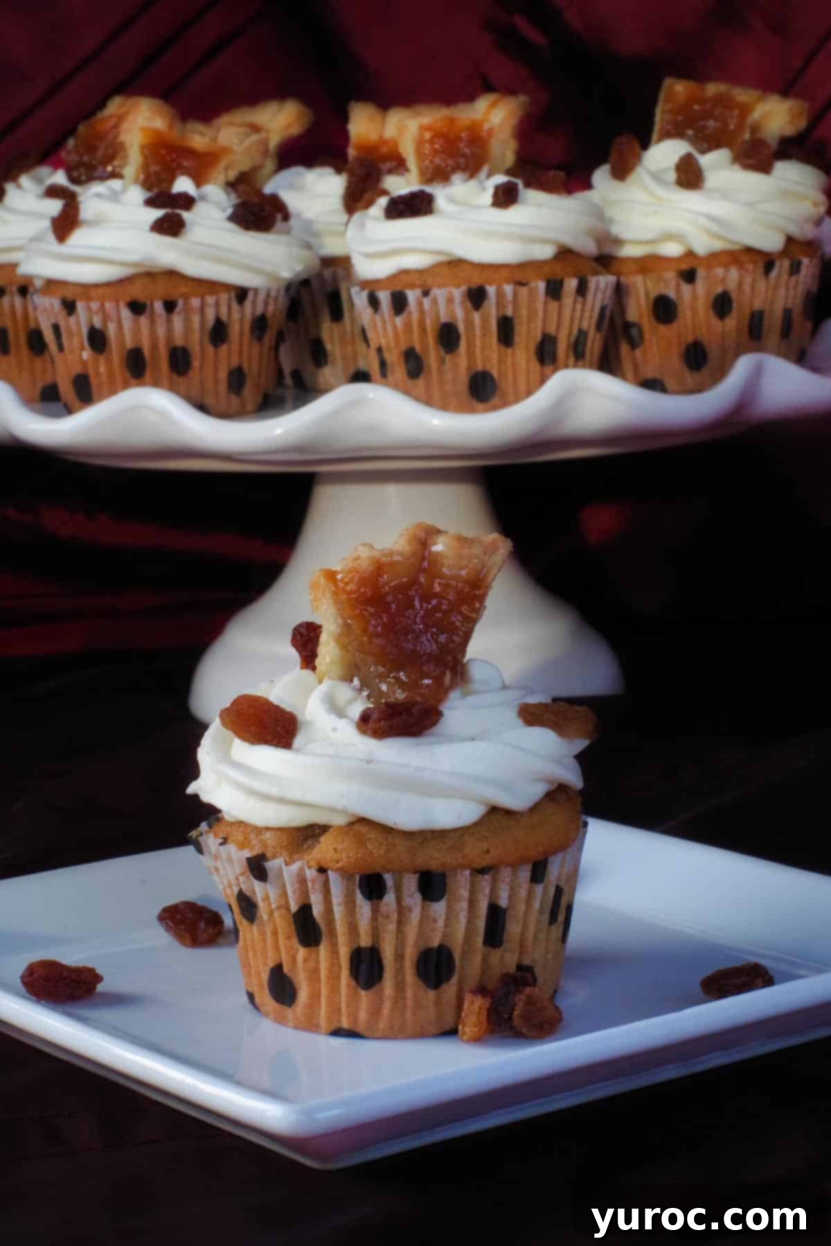 A butter tart cupcake on a white plate, with a platter of more cupcakes in the background