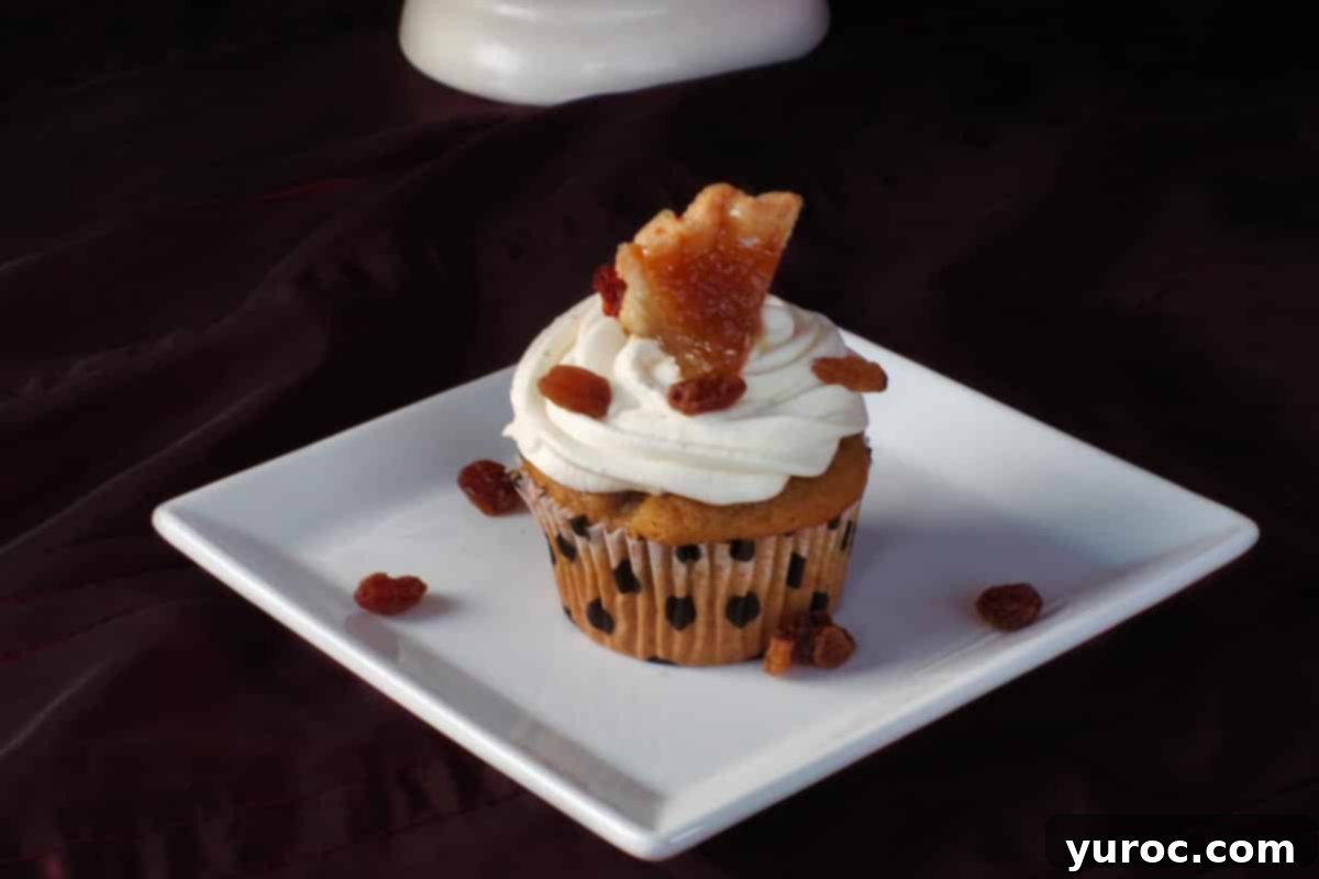 A single butter tart cupcake on a white plate, surrounded by scattered raisins