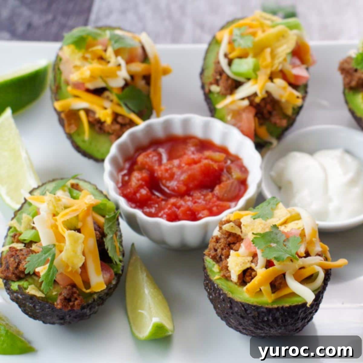a white tray of avocado tacos with salsa and sour cream in the middle and lime wedges on the side