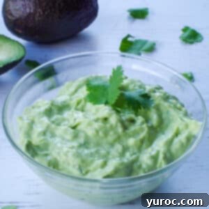 avocado cream sauce in a glass bowl with an avocado in the background
