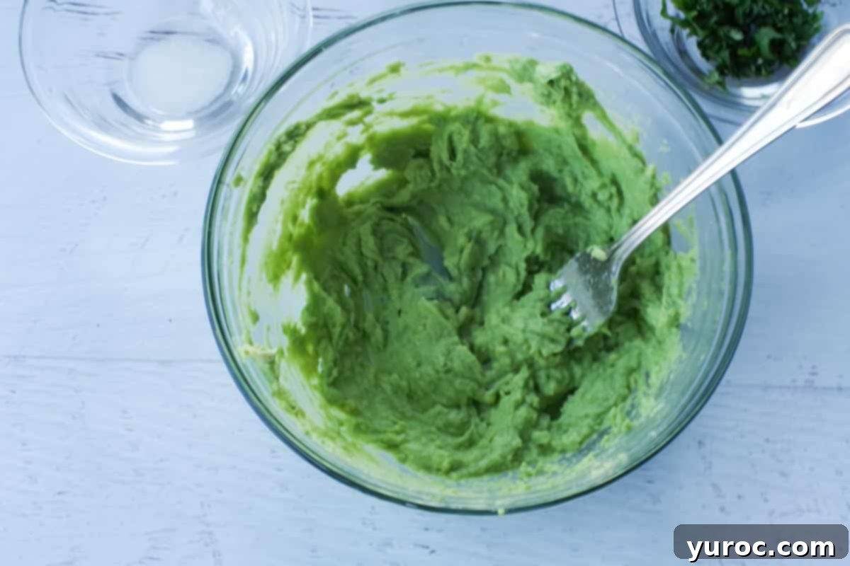 avocado being mashed with a fork, in a glass bowl