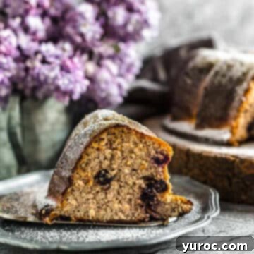A beautifully baked blueberry bundt cake resting on a plate, with delicate purple flowers subtly blurred in the background, creating a charming scene.