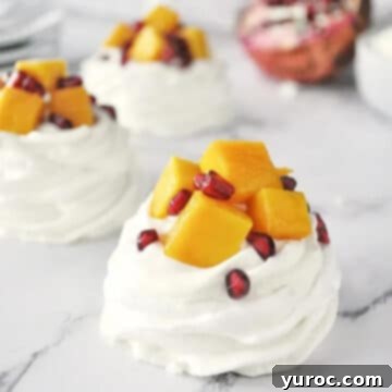 A delicate meringue nest beautifully filled with mango, pomegranate, and a creamy farmers cheese mixture, with more nests visible in the background.