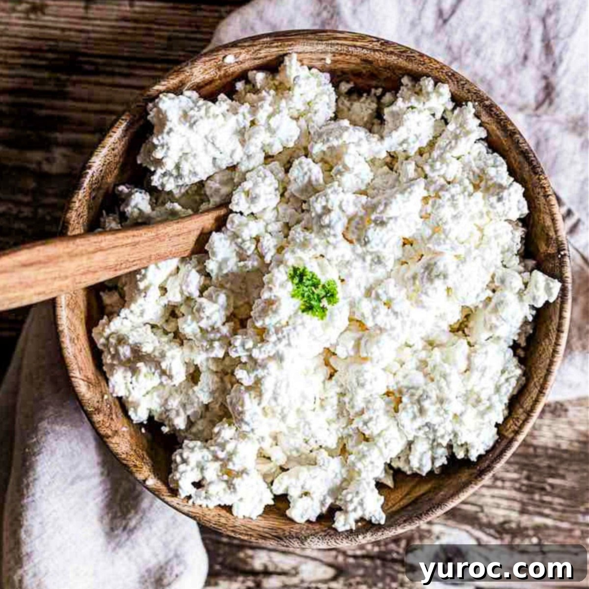 Homemade farmer's cheese in a rustic brown bowl, with a spoon resting in it, showcasing its crumbly texture.