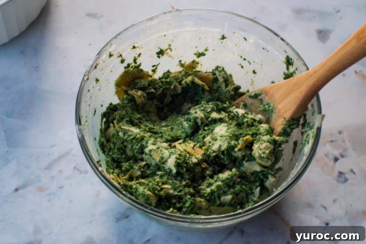 spinach artichoke mixture in large glass bowl with wooden spoon
