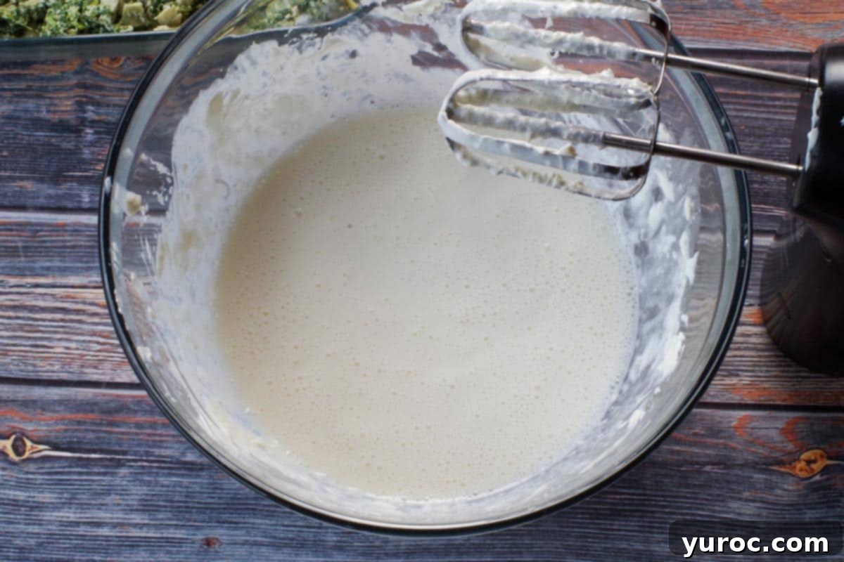 cream cheese beaten with milk in glass bowl with beaters over bowl