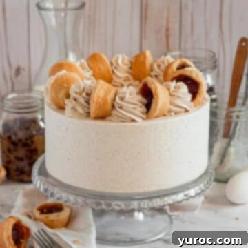 A magnificent butter tart layer cake displayed on an elegant glass cake stand, flanked by two individual butter tarts and sophisticated glassware in the soft-focus background