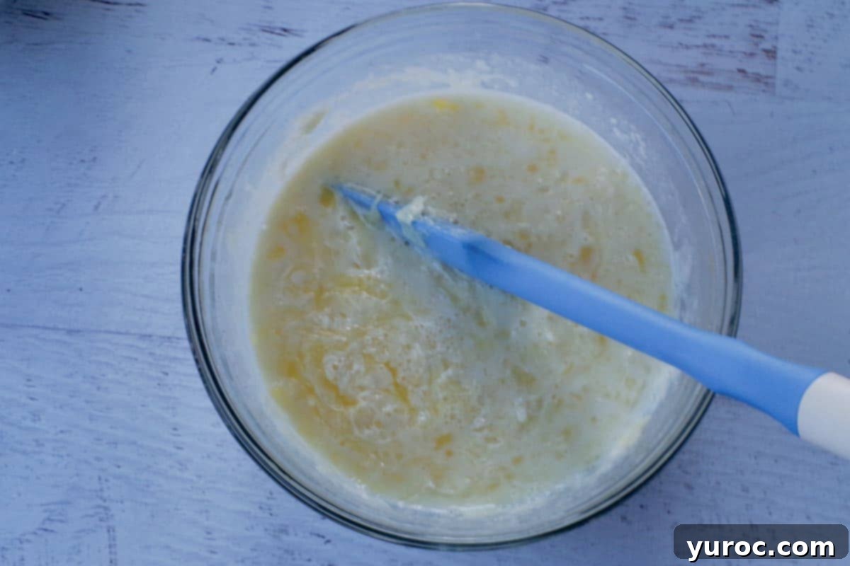 wet ingredients mixed together in medium glass bowl, with blue spatula