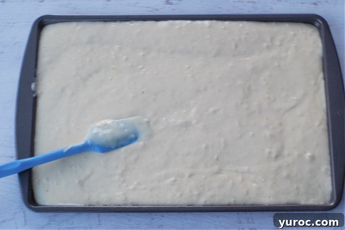 pancake batter poured onto sheet pan with blue spatula spreading it