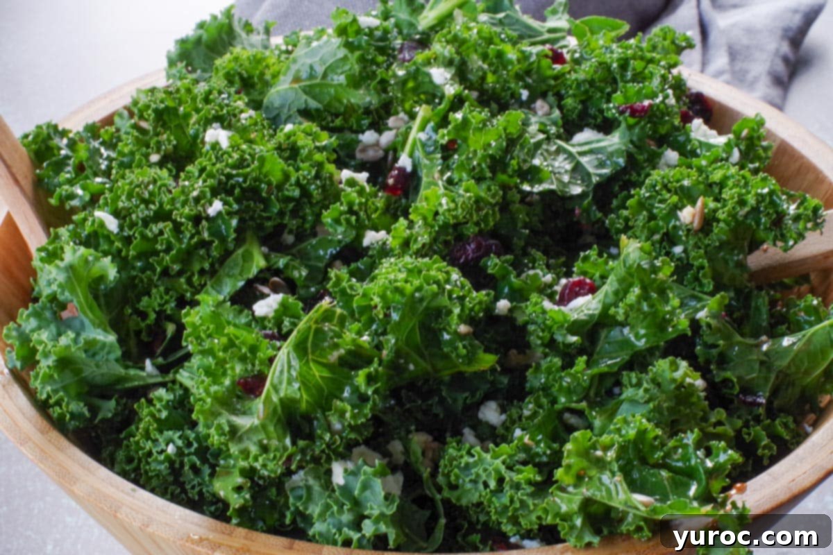 close up shot of kale salad in wooden bowl with wooden utensils
