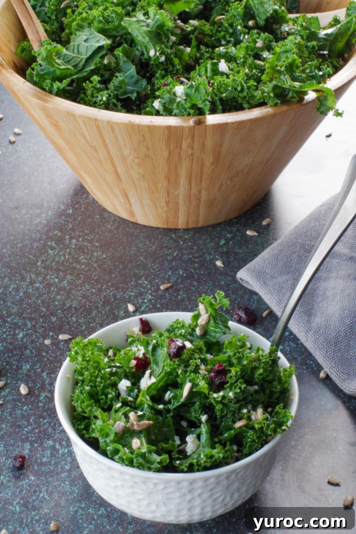 kale salad in small white bowl in front of more salad in large wooden bowl in background