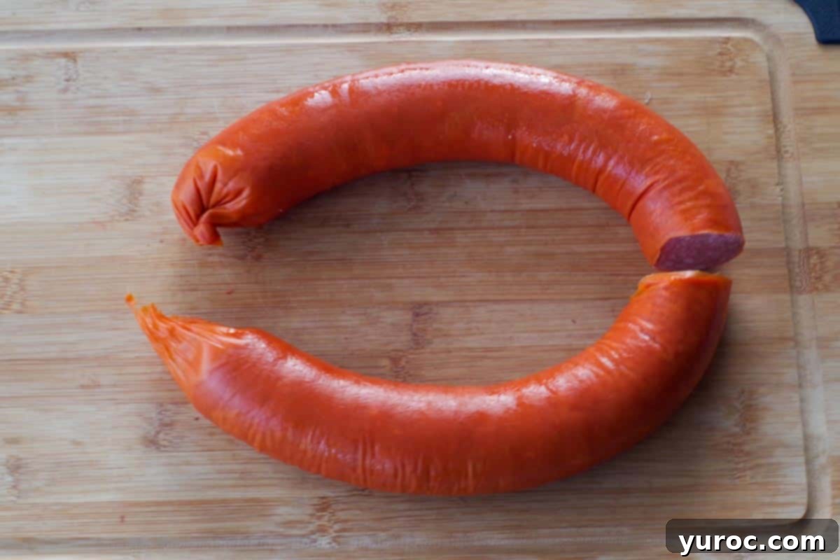Kielbasa ring cut in half on a wooden cutting board, ready for casing removal