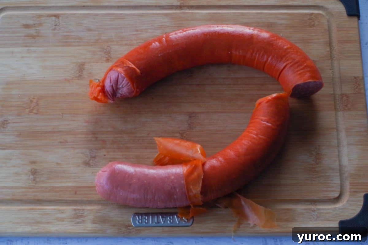 Casing on kielbasa pulled back, partially removed, on a wooden cutting board