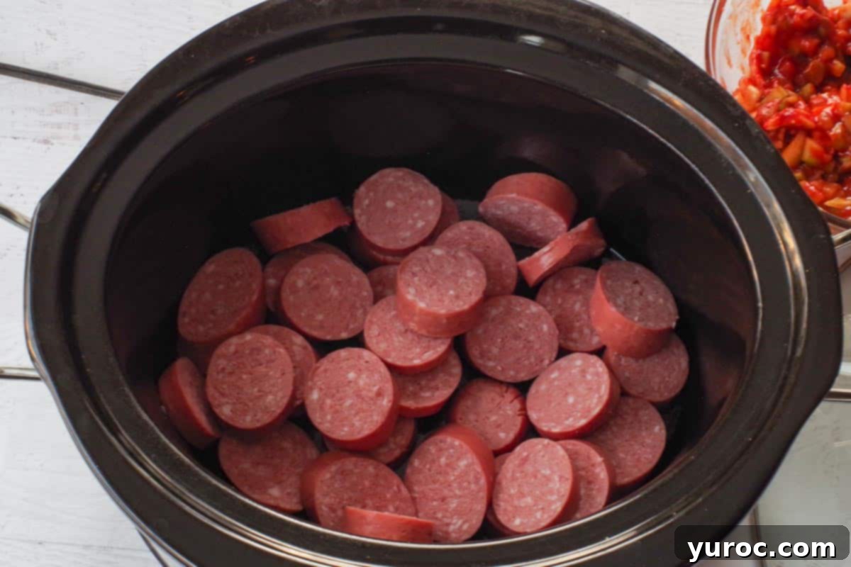 Sliced kielbasa pieces arranged in the bottom of a slow cooker