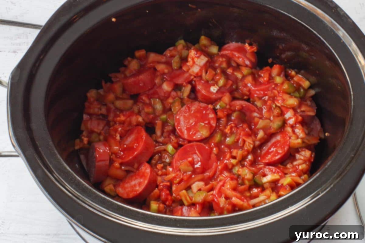 Mixed sauce ingredients poured evenly over kielbasa pieces in slow cooker